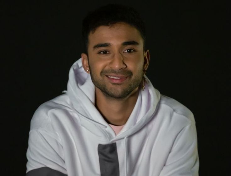 a man in a white hoodie and tie smiling at the camera with his arms crossed