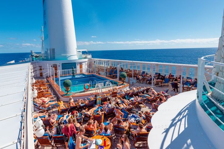 people are sitting on the deck of a cruise ship with a pool and lighthouse in the background