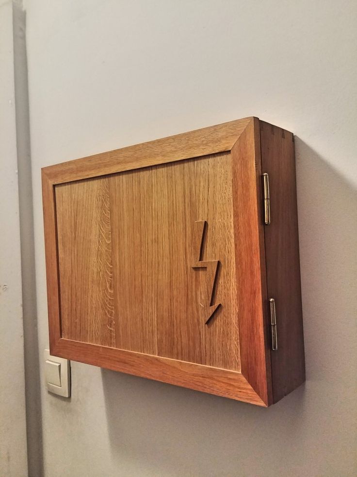 a wooden clock mounted to the side of a wall next to a light switch on a white wall