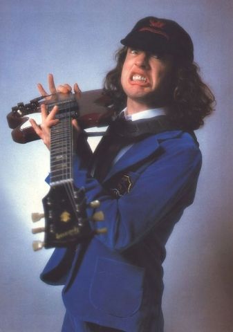 a man with long hair holding a guitar in his right hand and smiling at the camera