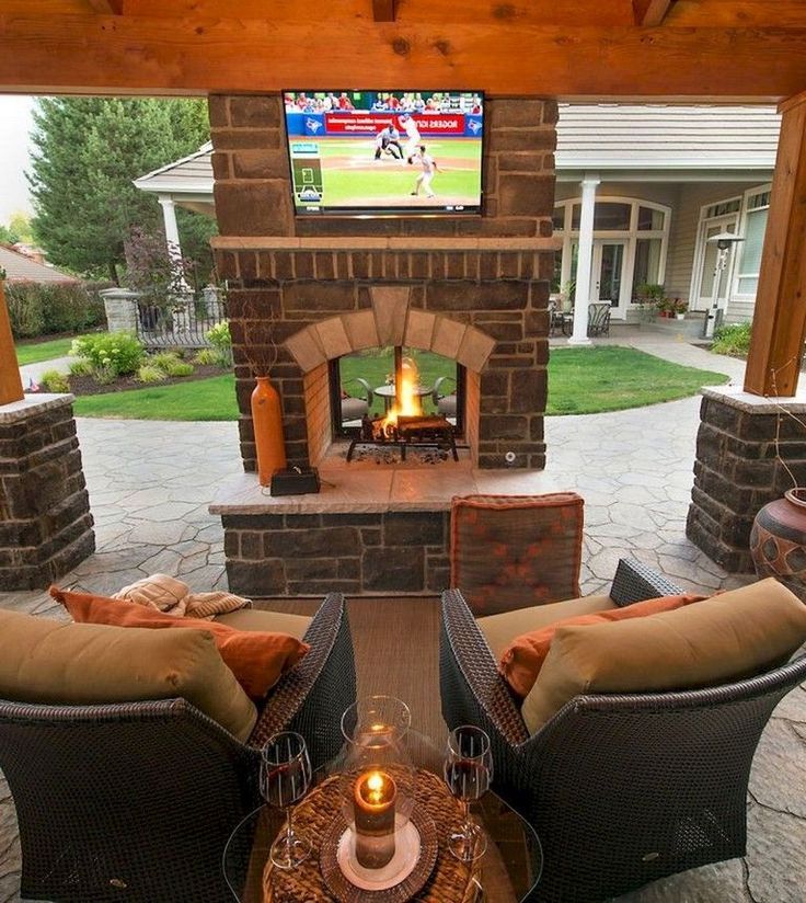 an outdoor fireplace with two couches and a television on the wall in front of it