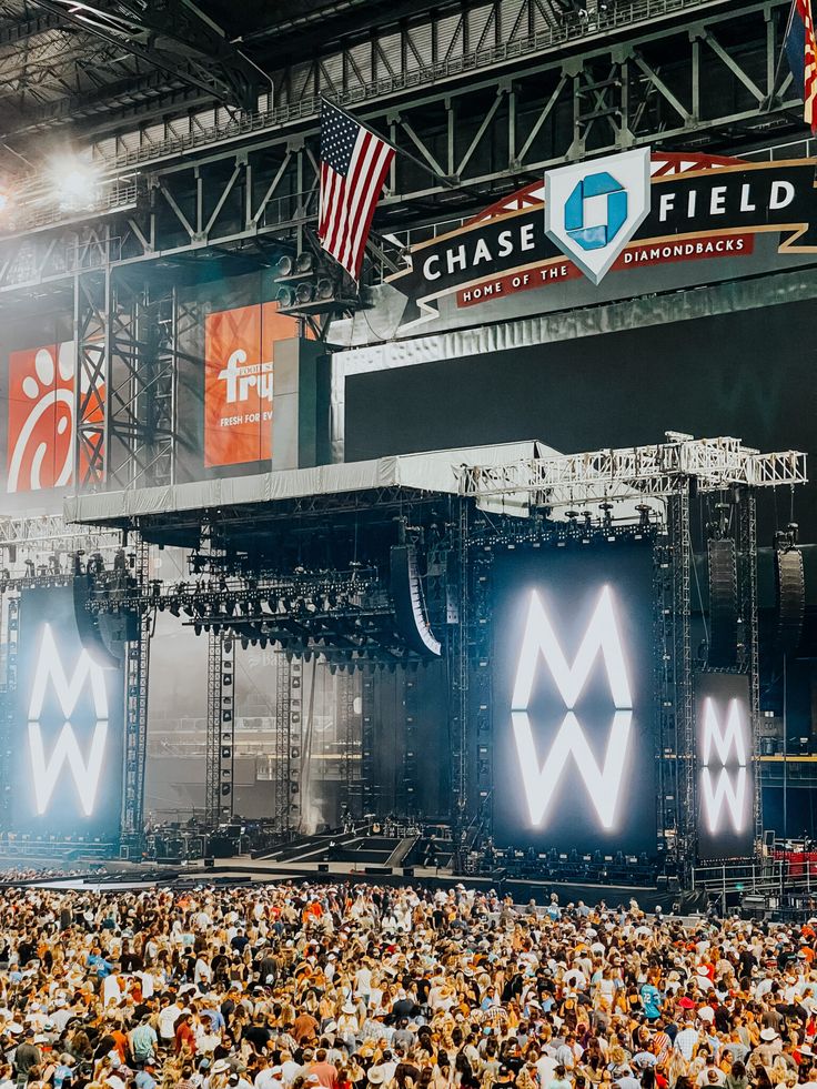 a large group of people at a concert with stage lights and american flags in the background