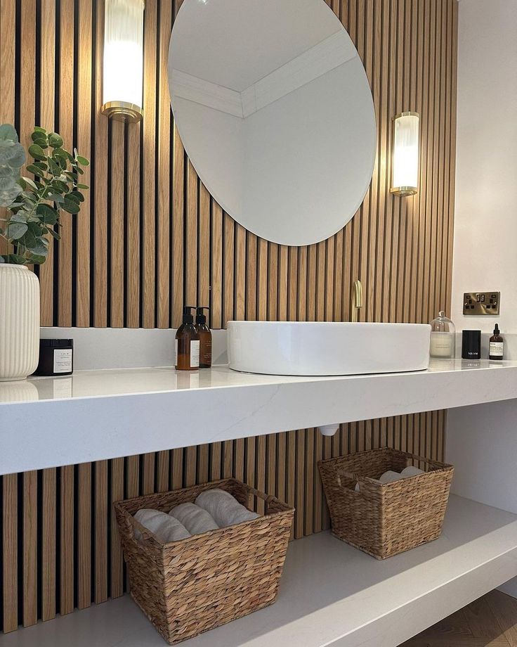 a white sink sitting under a bathroom mirror next to a wooden shelf with baskets on it