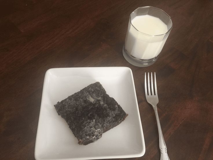 a square white plate with some food on it next to a glass of milk and a fork