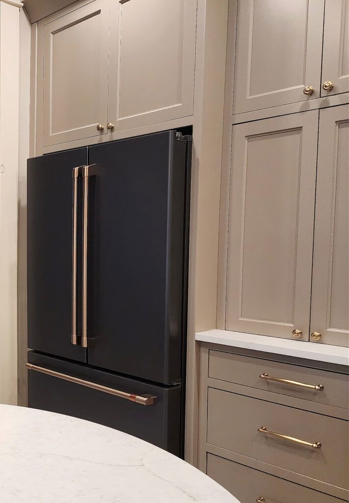 a black refrigerator freezer sitting inside of a kitchen next to white counter tops and cabinets