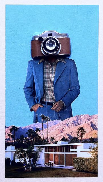 a man with a camera on his head standing in front of a house and palm trees