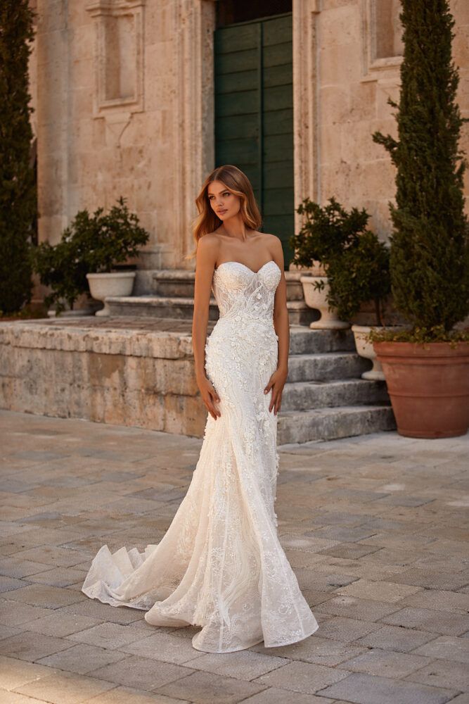 a woman in a white wedding dress standing on a stone walkway with potted plants behind her