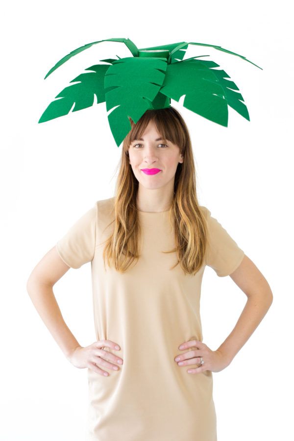 a woman standing with her hands on her hips wearing a paper palm tree headpiece