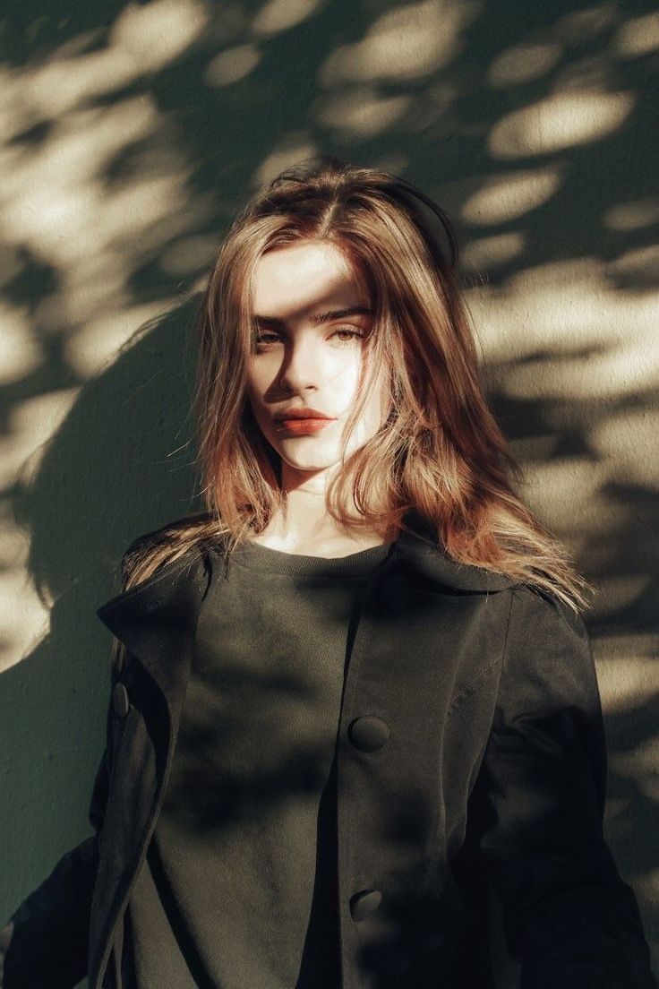 a woman standing in front of a wall wearing a black coat and red lipstick with long hair