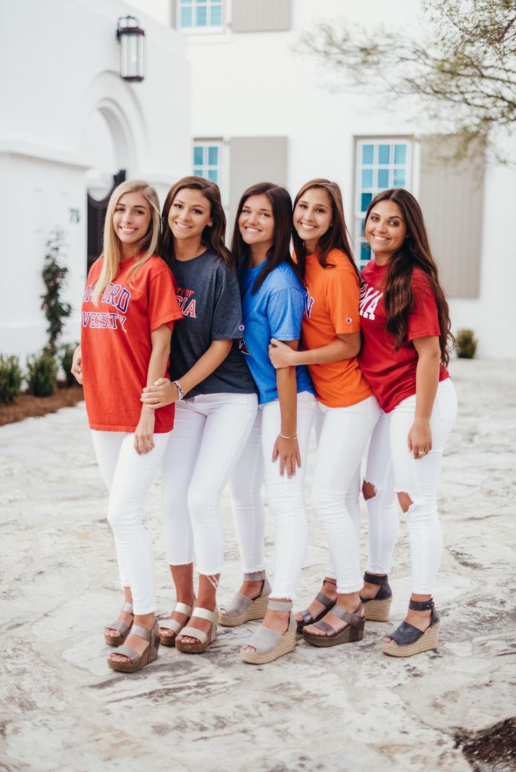 four girls standing in front of a white house wearing orange and blue t - shirts