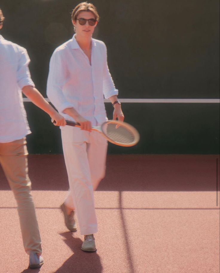 two people holding tennis racquets walking on a tennis court in the sun