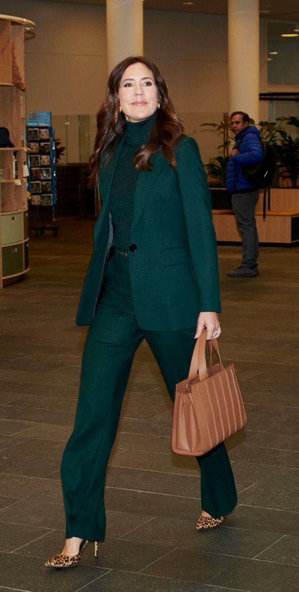 a woman in a green suit is carrying a brown bag and walking through an airport