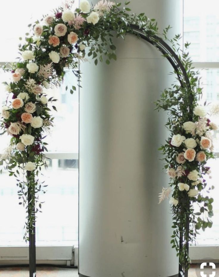 an arch decorated with flowers and greenery stands in front of a window at the end of a room