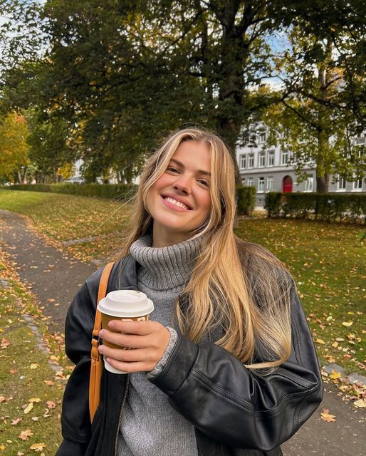 a woman is walking down the street with her coffee in her hand and smiling at the camera