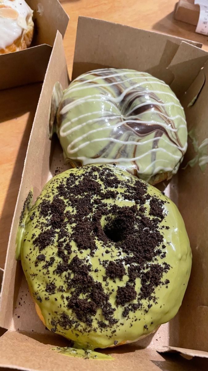 two donuts with green icing and chocolate sprinkles in a box