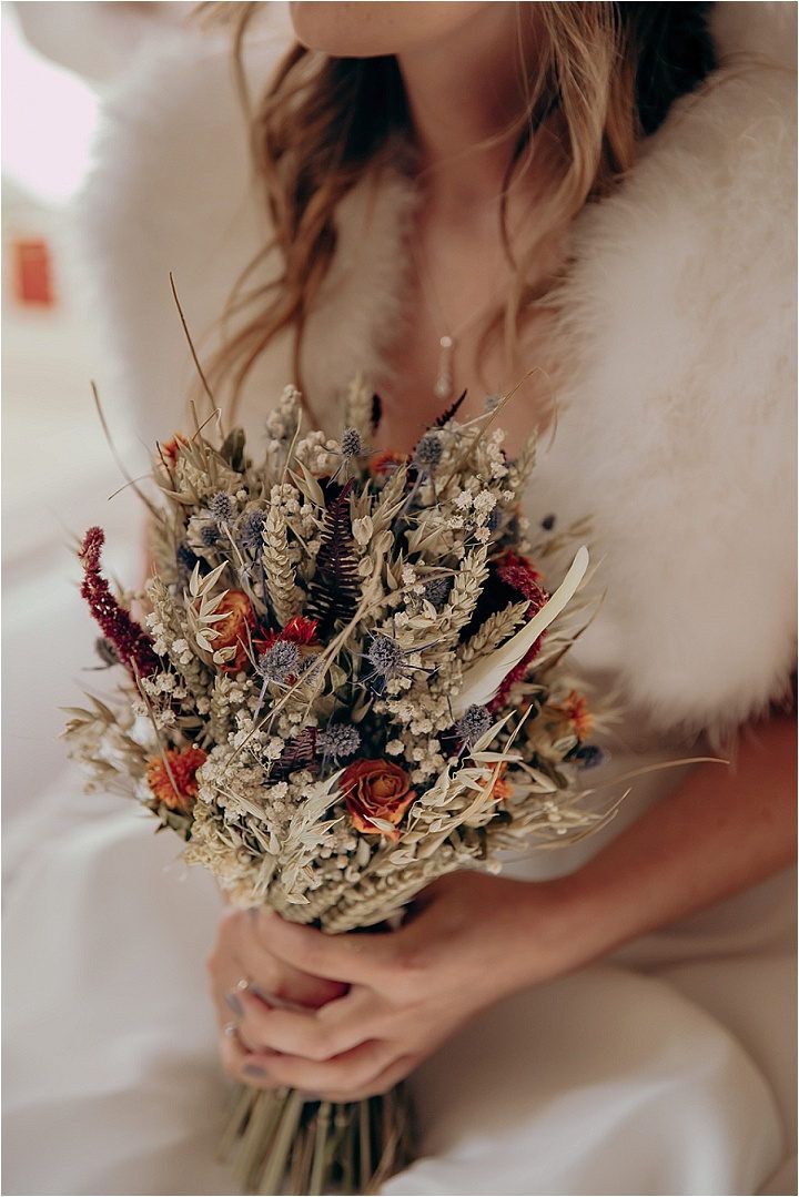 a woman wearing a fur coat holding a bouquet of dried flowers in her left hand