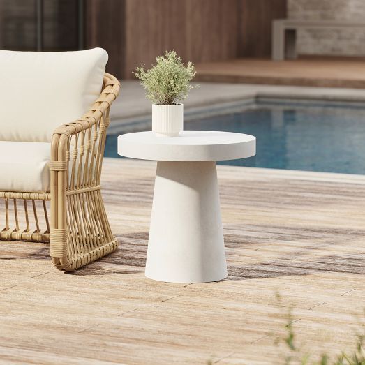 a wicker chair next to a table with a potted plant on it near a pool