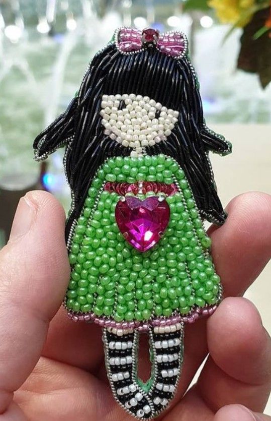 a hand holding a small beaded doll with a heart on it's chest