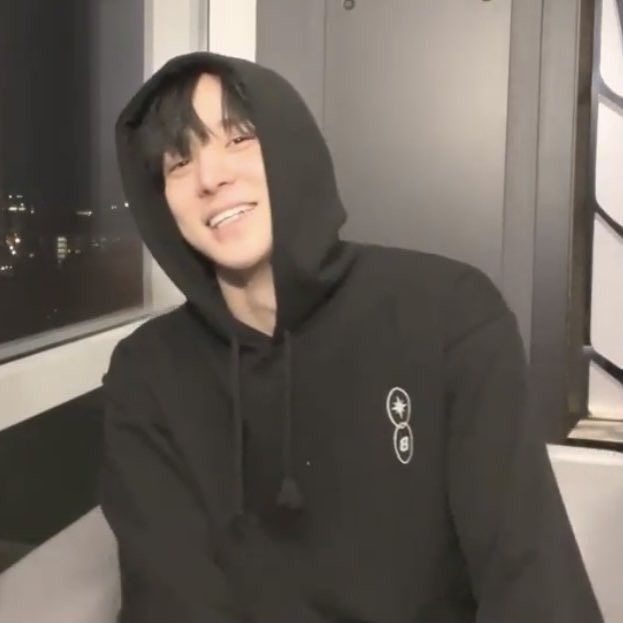 a young man in a black hoodie is smiling and looking at the camera while sitting down