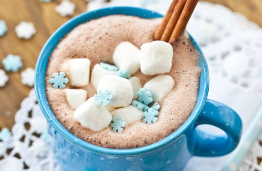 hot chocolate with marshmallows and cinnamon in a blue mug on a doily