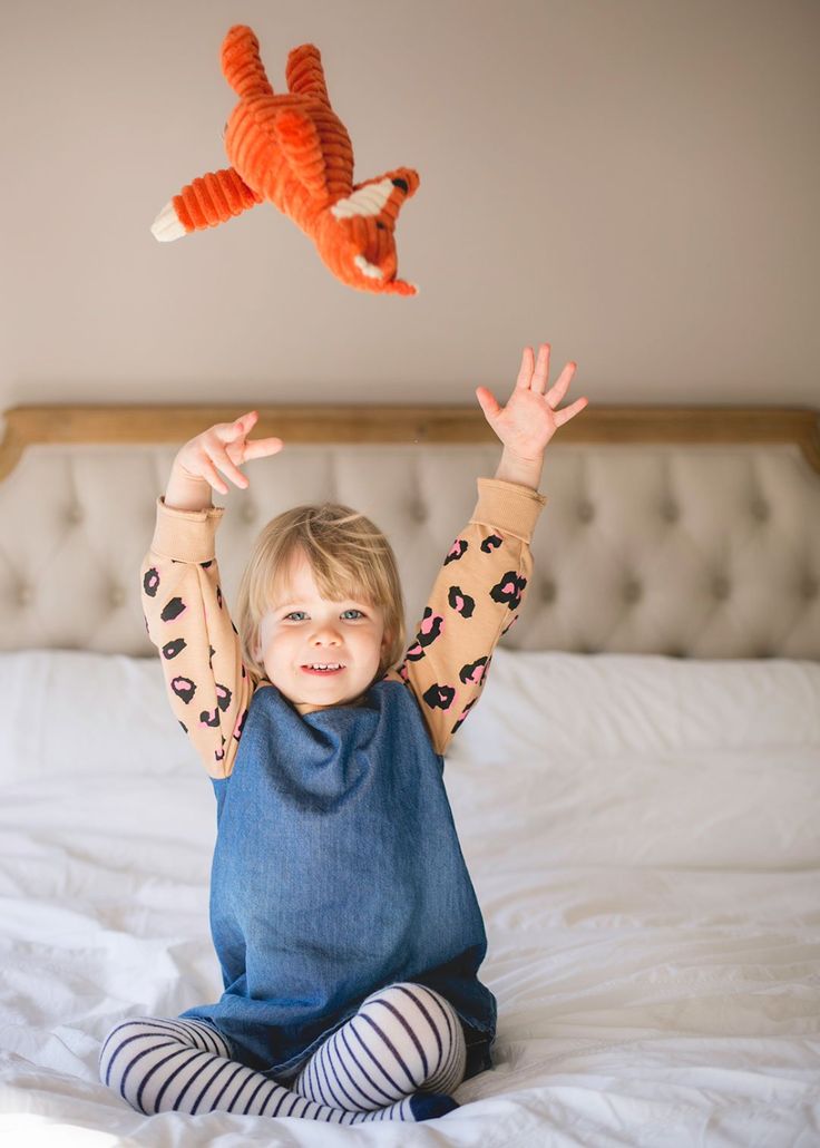 a little boy sitting on top of a bed holding two stuffed animals in the air