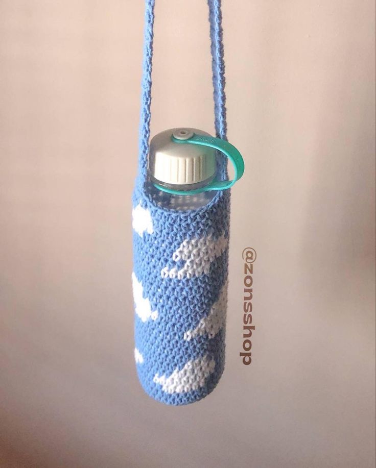 a blue and white crocheted water bottle holder hanging from a hook on a wall