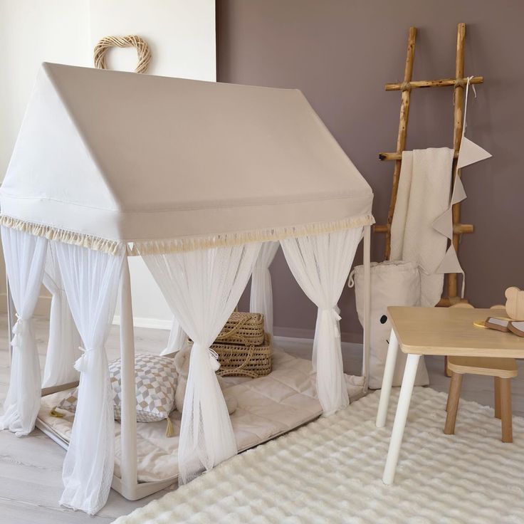 a white bed with curtains and pillows on top of it next to a wooden table