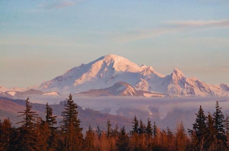 the mountains are covered with clouds and trees in the foreground, while the sun is low on the horizon