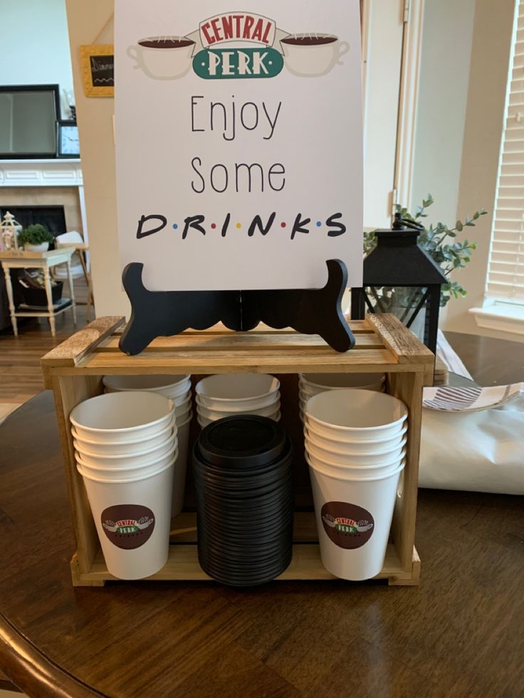 there is a sign that says enjoy some drinks on the table with cups in front of it