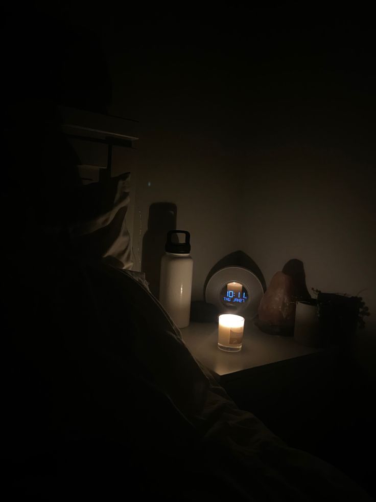 a lit candle sitting on top of a table next to a vase and bottle in the dark