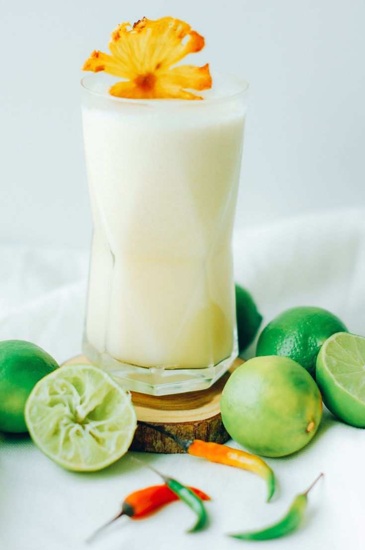 a glass filled with milk surrounded by limes and peppers