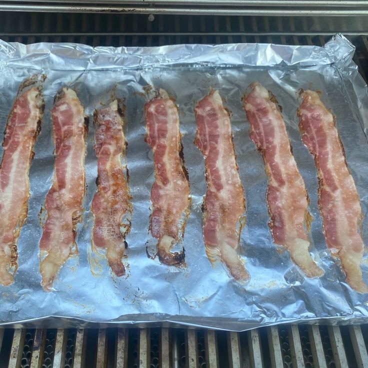 bacon is being cooked on the grill with aluminum foil