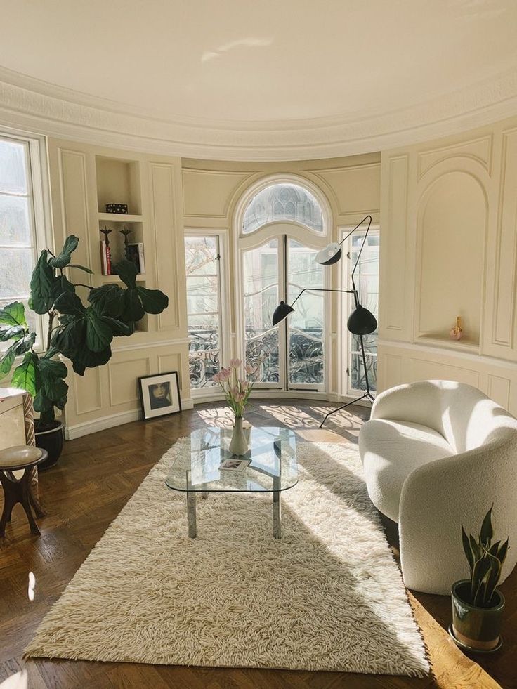 a living room filled with white furniture and lots of plants on top of a hard wood floor