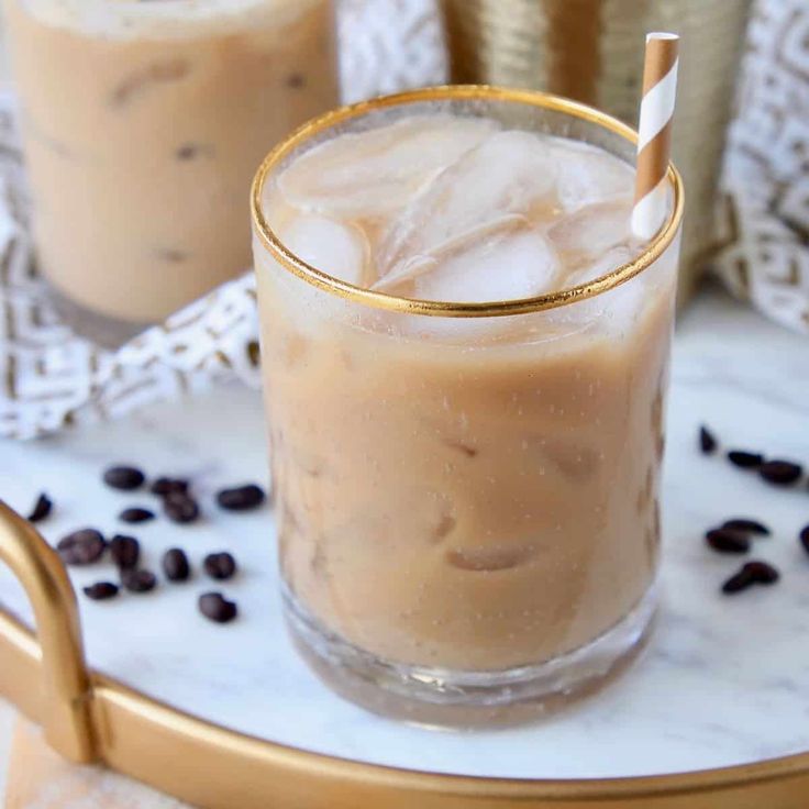 two glasses filled with iced coffee on top of a white and gold serving platter