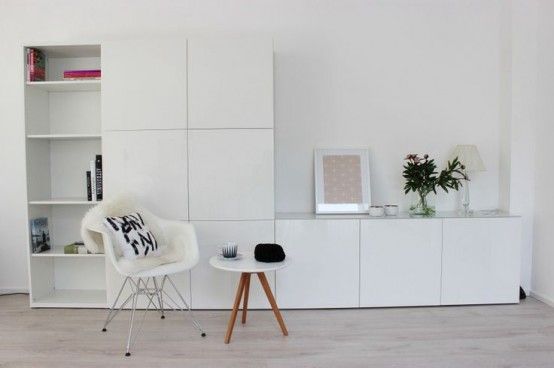 a living room with white furniture and bookshelves on the wall next to a small table