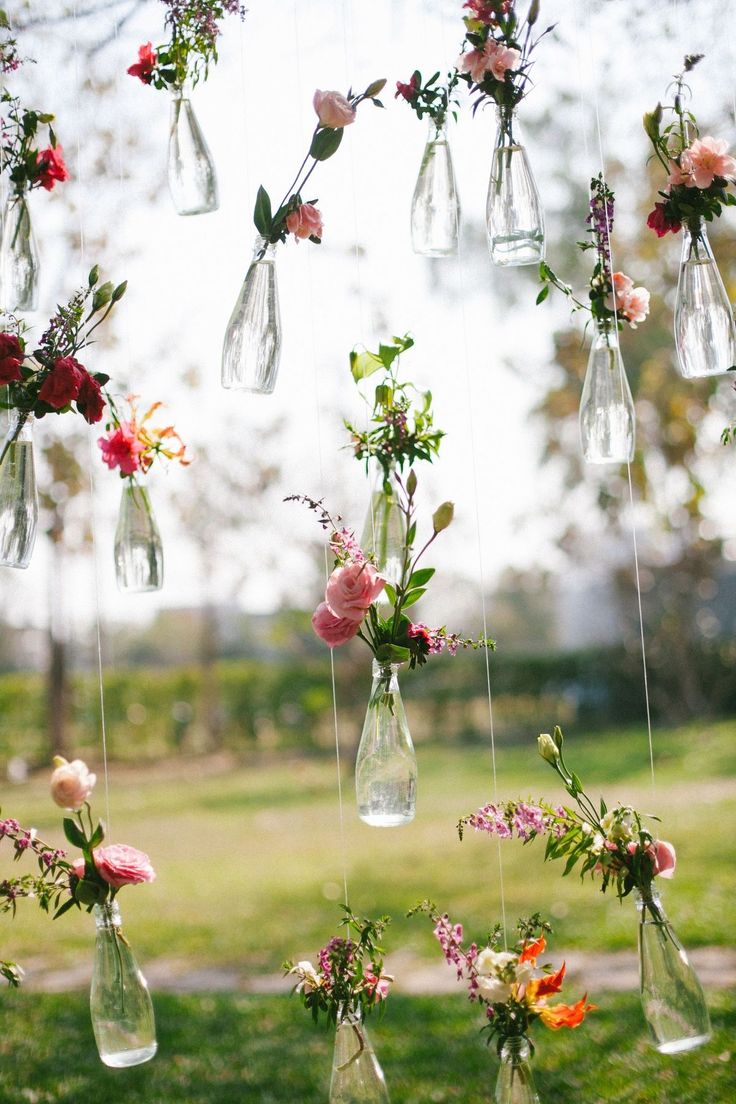 several vases filled with flowers hanging from strings in the grass near a park area