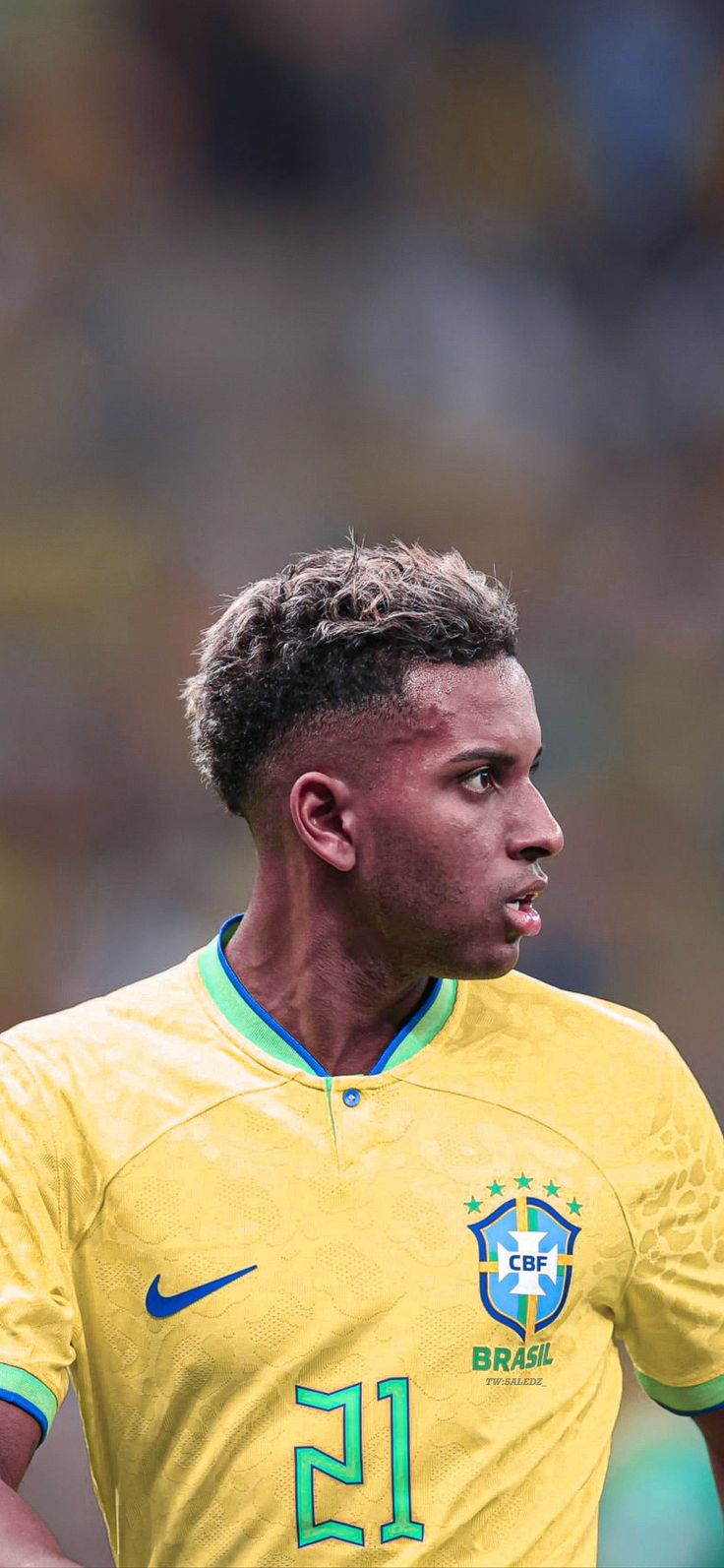 a soccer player is looking down at the ball in his hand while wearing a yellow uniform