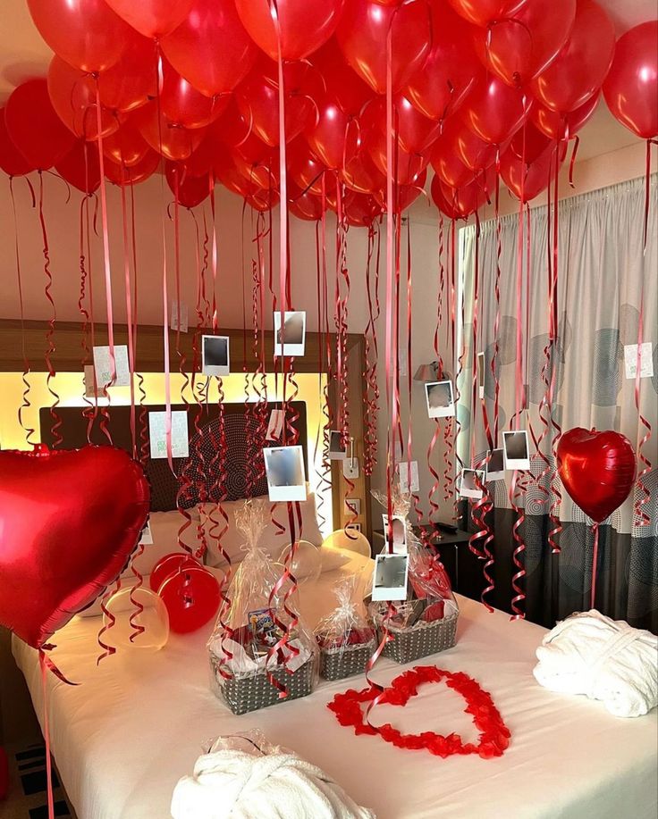 red balloons are hanging from the ceiling above a bed with white sheets and pillows on it