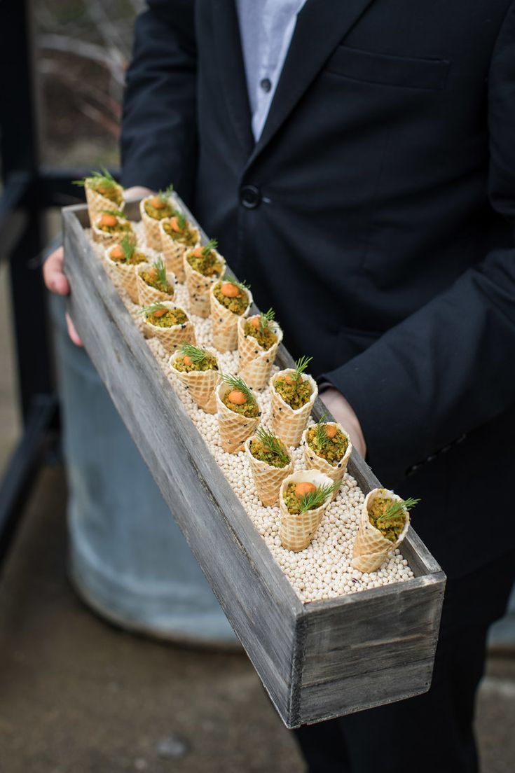 a man in a suit holding a tray filled with small cups and plants on it