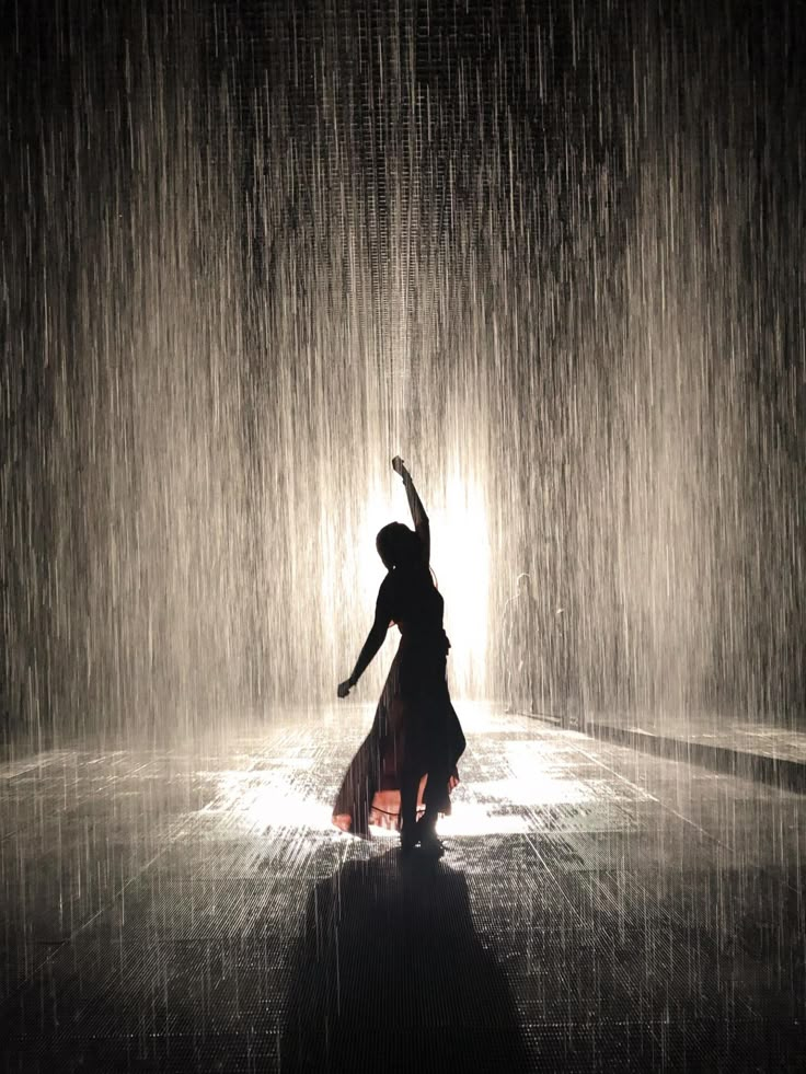 a woman is dancing in the rain with her arms up and hands raised above her head