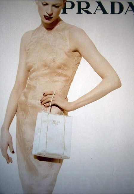 a woman holding a white bag standing in front of a prada advertisement