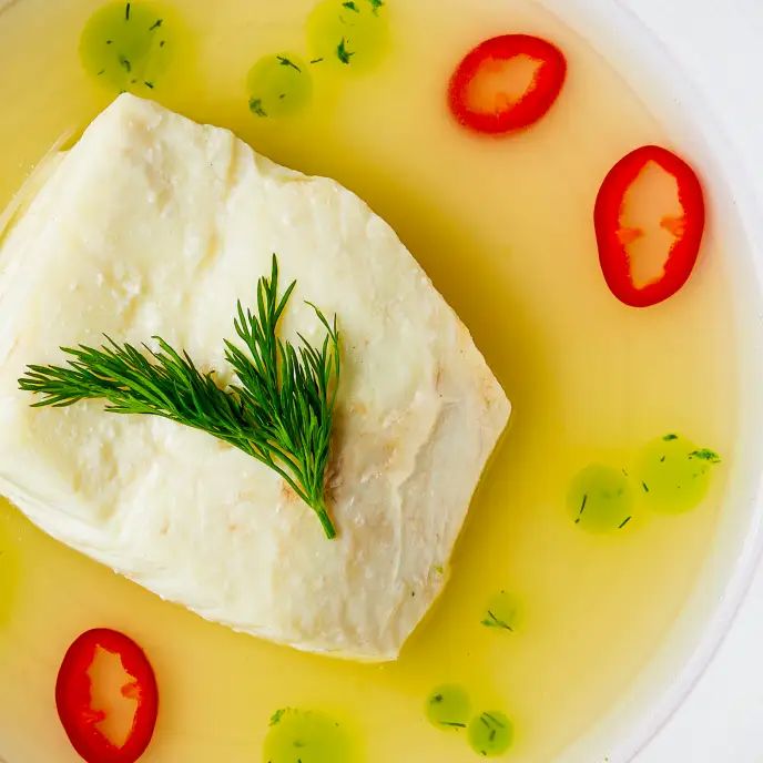 a piece of fish is in a bowl with tomatoes and green garnish on the side