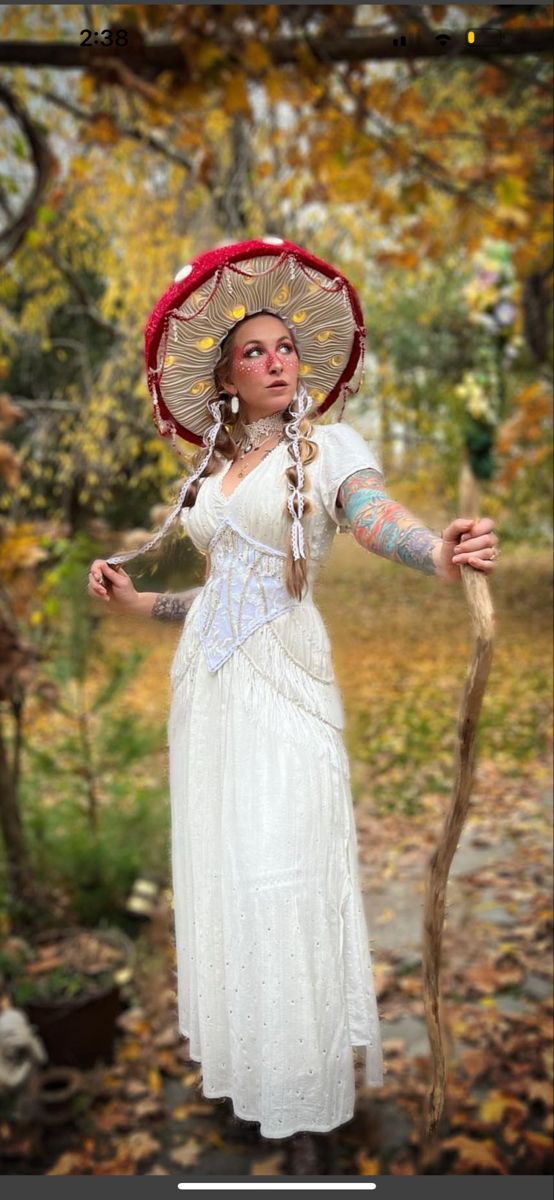 a woman in a white dress and red hat holding a stick with her right hand