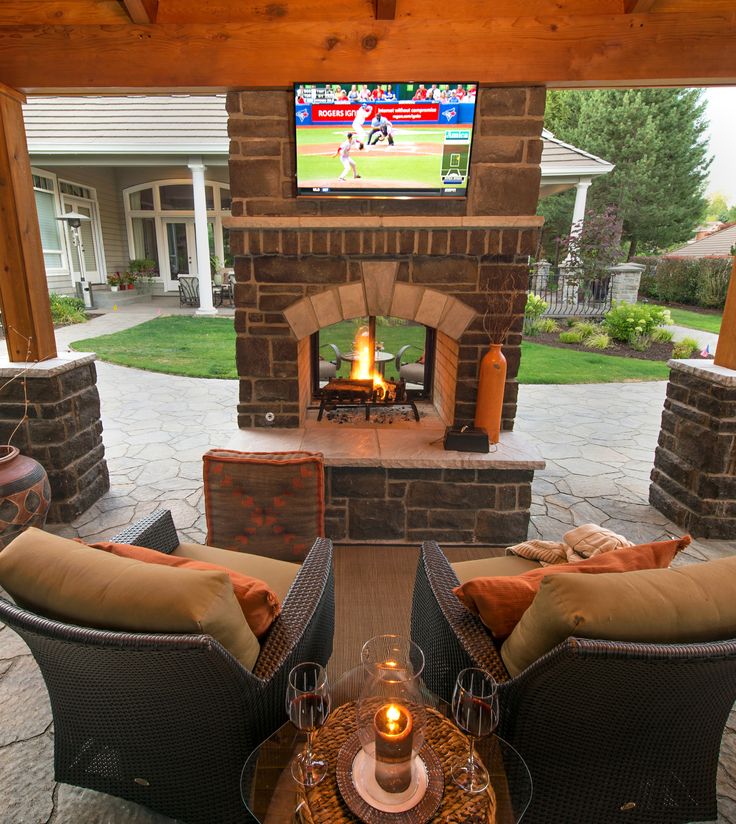 an outdoor fireplace with two couches and a television on the wall in front of it