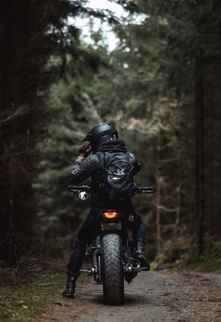 a man riding on the back of a motorcycle down a dirt road through a forest