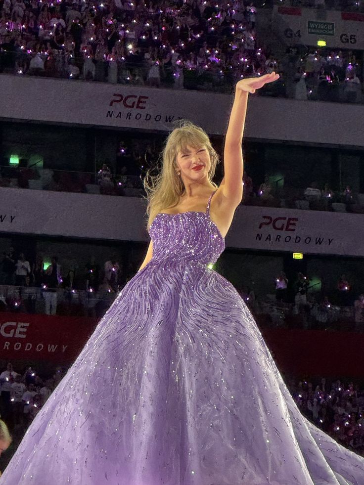 a woman in a purple dress standing on top of a stage with her arms up