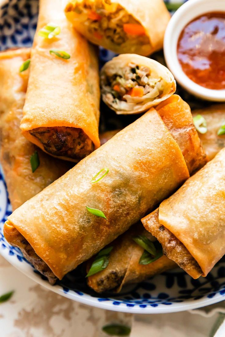 a plate filled with meat and vegetable spring rolls next to dipping sauce on the side