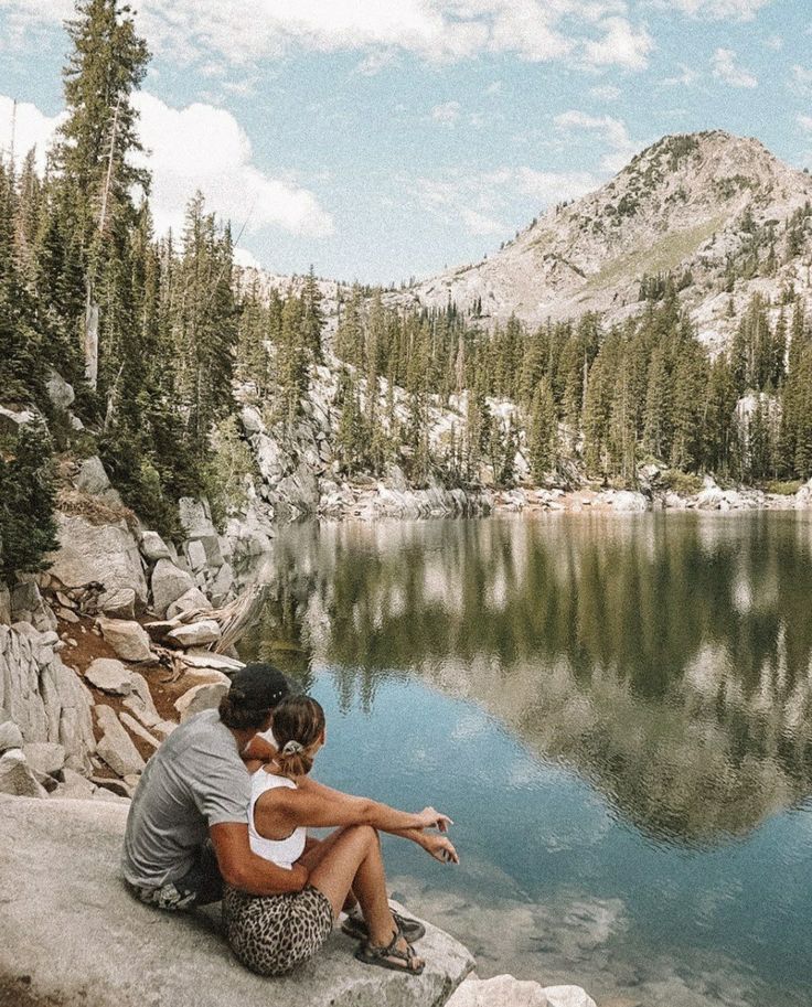 a man and woman sitting on the edge of a lake