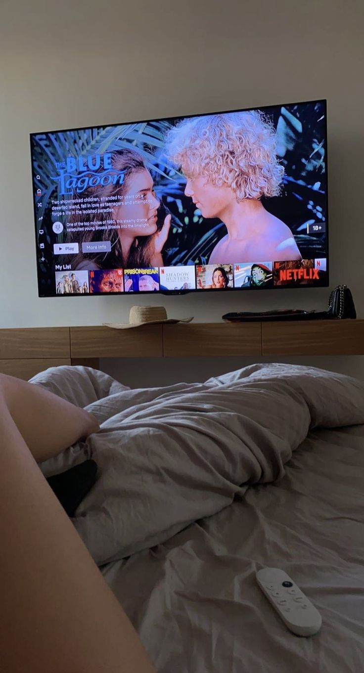 a woman laying in bed watching tv with her legs crossed