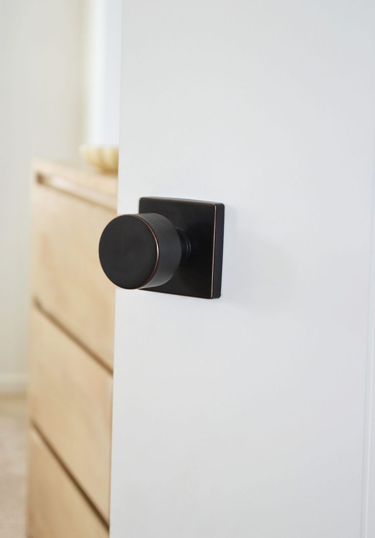 a black knob on the side of a white wall next to a wooden dresser with drawers